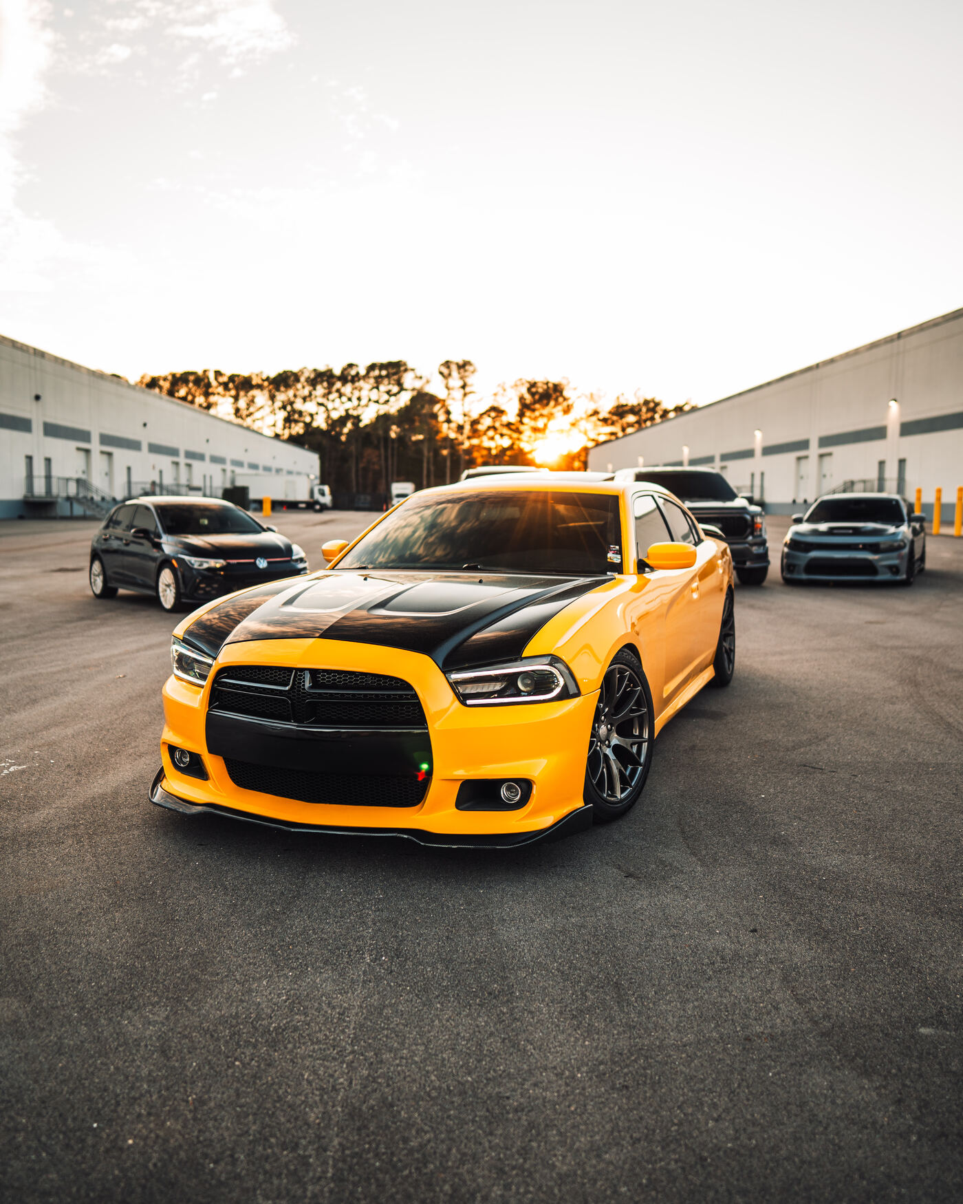 Yellow Dodge Charger front at sunset warehouse with GTI and grey Hellcat