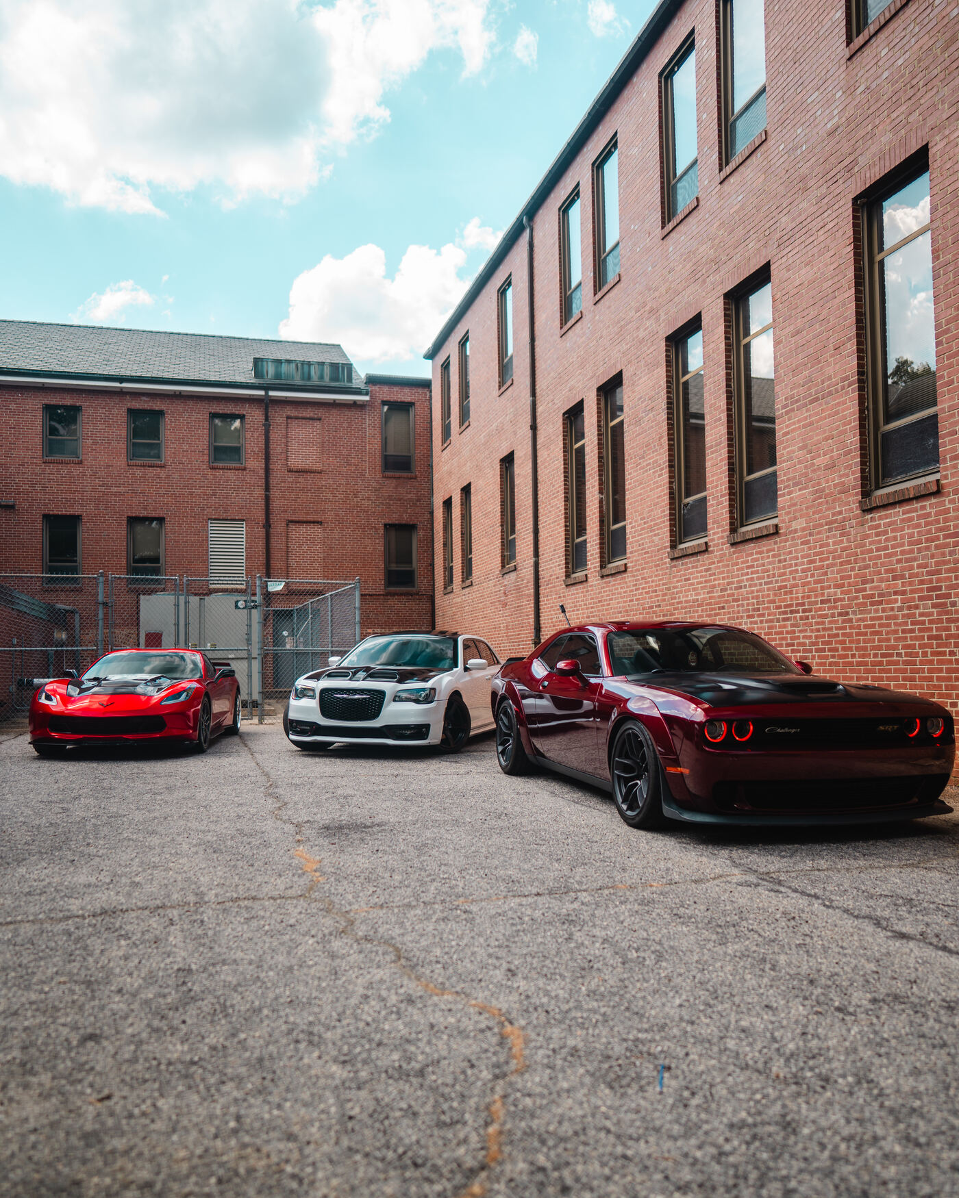 Red Corvette, white Chrysler 300 and burgundy Challenger lined up in urban alley