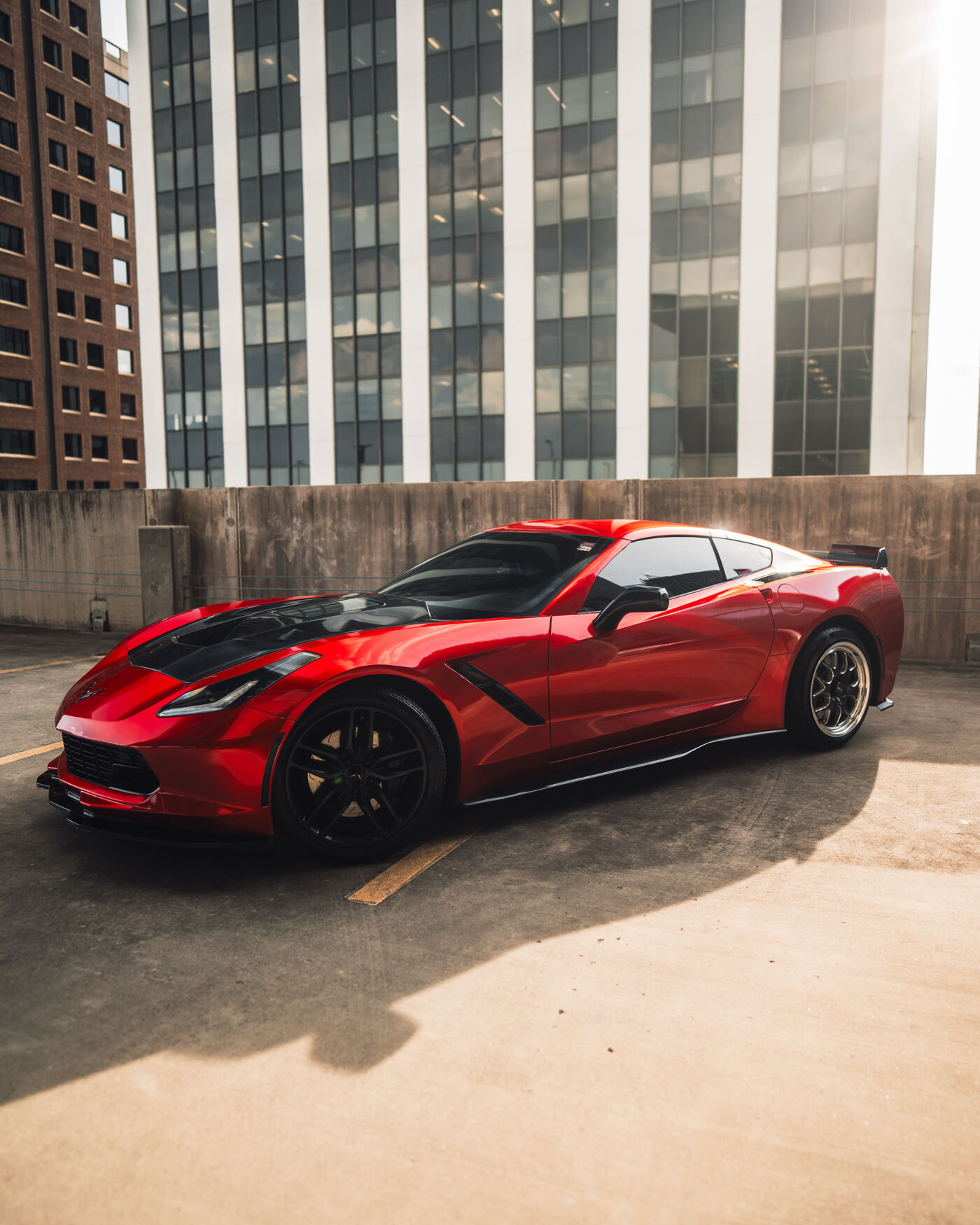 Red C7 Corvette side profile on rooftop with city skyline